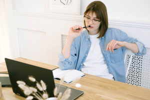 woman in denim jacket thinking with her pen in mouth
